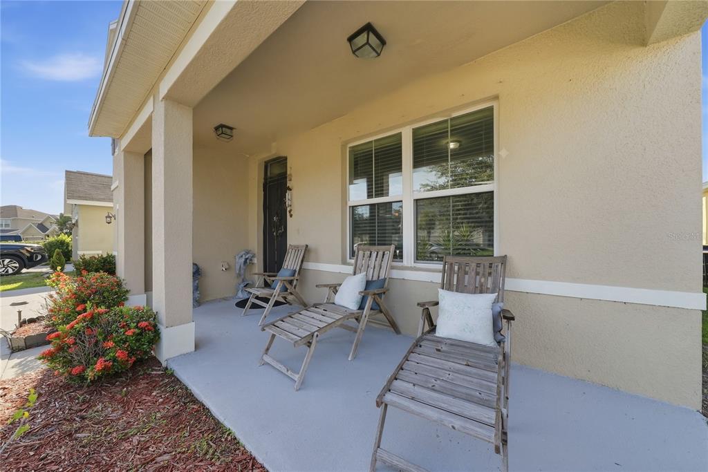 A covered front porch features a concrete floor, two wooden lounge chairs, and a window — 8128 HARWICH PORT LANE, GIBSONTON, FL