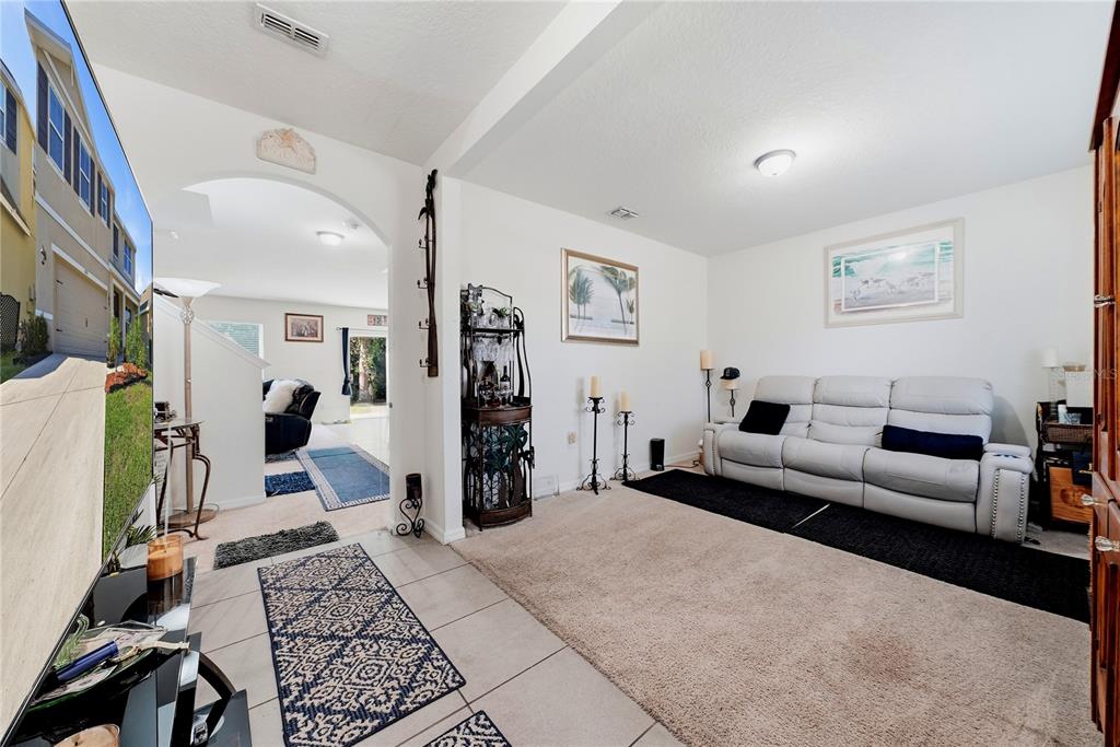 A living room features a white sofa, beige carpet, tile flooring, and an arched entryway — 8128 HARWICH PORT LANE, GIBSONTON, FL