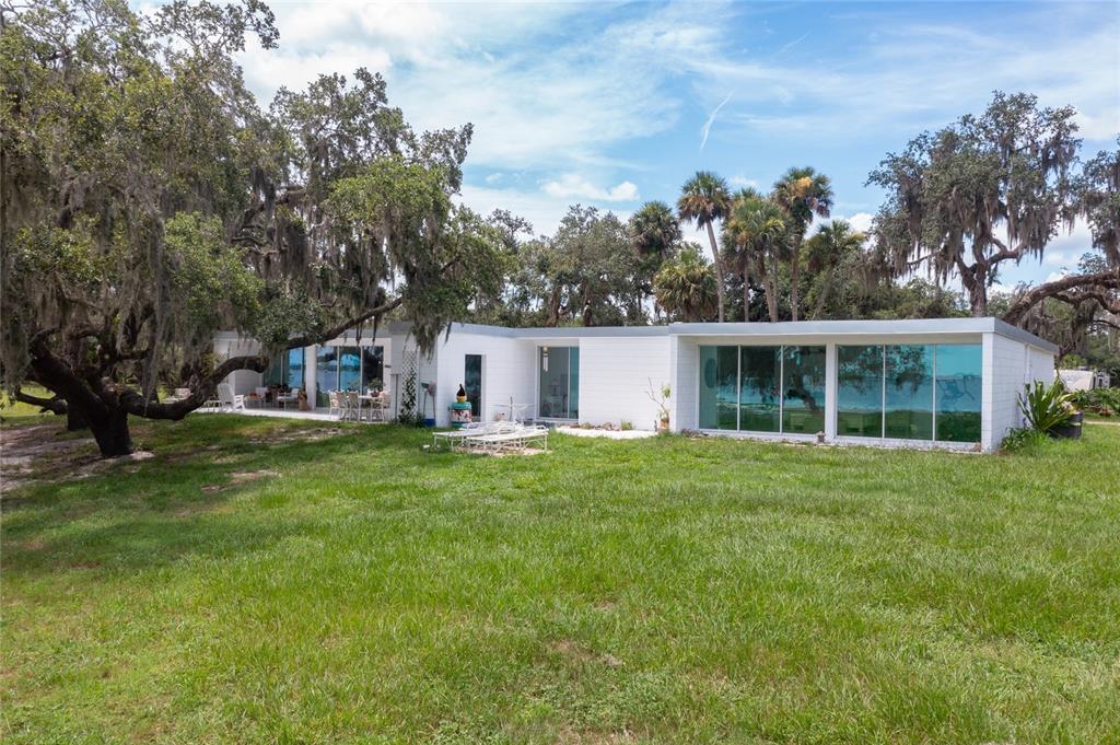 A single-story white house with large glass windows sits on a grassy lawn with trees — 2600 FORT LANE ROAD, GENEVA, FL