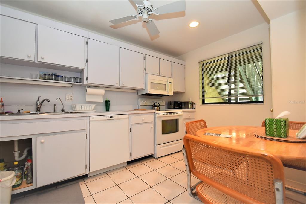 A kitchen with white cabinets, white appliances, a dining table, and tiled flooring — 1526 PELICAN POINT DRIVE UNIT BA144, SARASOTA, FL