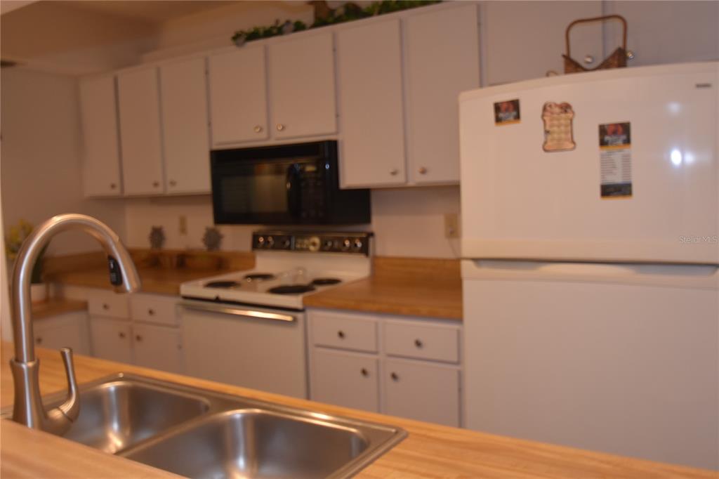 A kitchen features white cabinets, a white refrigerator, a black microwave, and a double sink — 1526 PELICAN POINT DRIVE UNIT BA144, SARASOTA, FL
