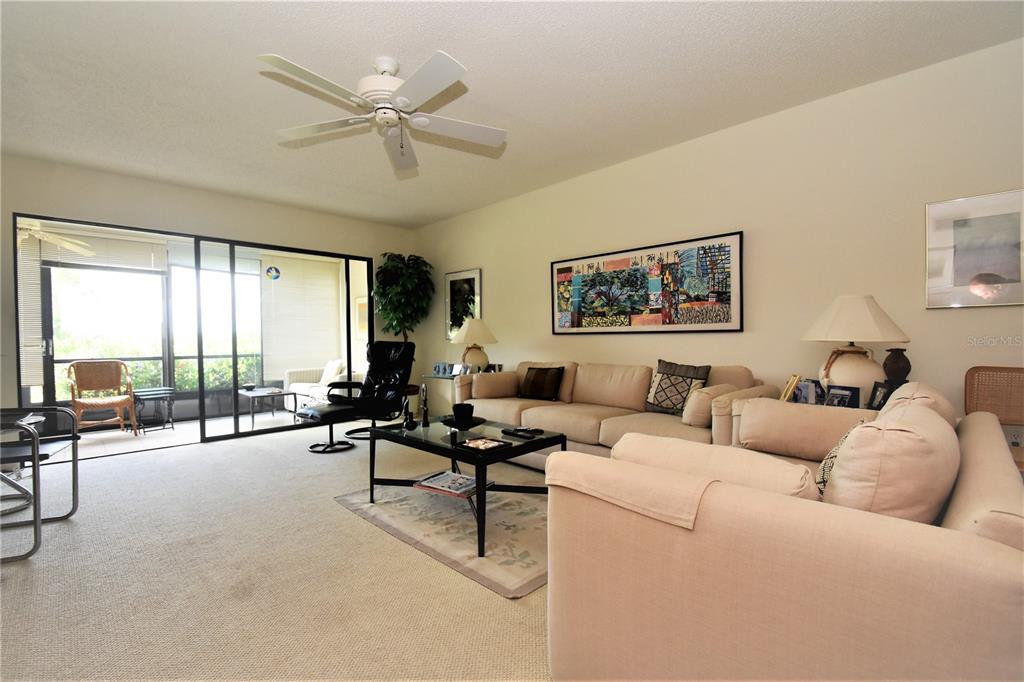 A living room features beige carpet, a ceiling fan, a large sectional sofa, and sliding doors — 1526 PELICAN POINT DRIVE UNIT BA144, SARASOTA, FL