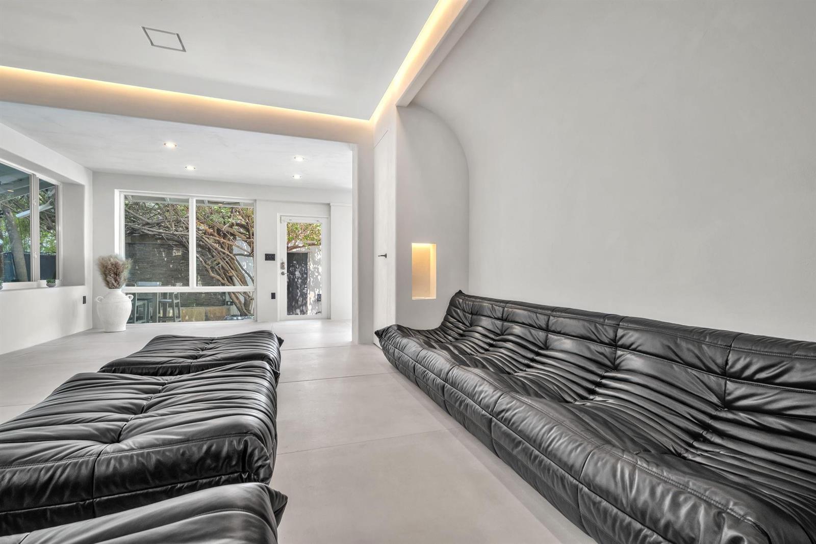 A modern living room features black tufted leather sofas, white walls, and recessed ceiling lighting — 120 NE 25th Street, Miami FL 33137, MIAMI, FL