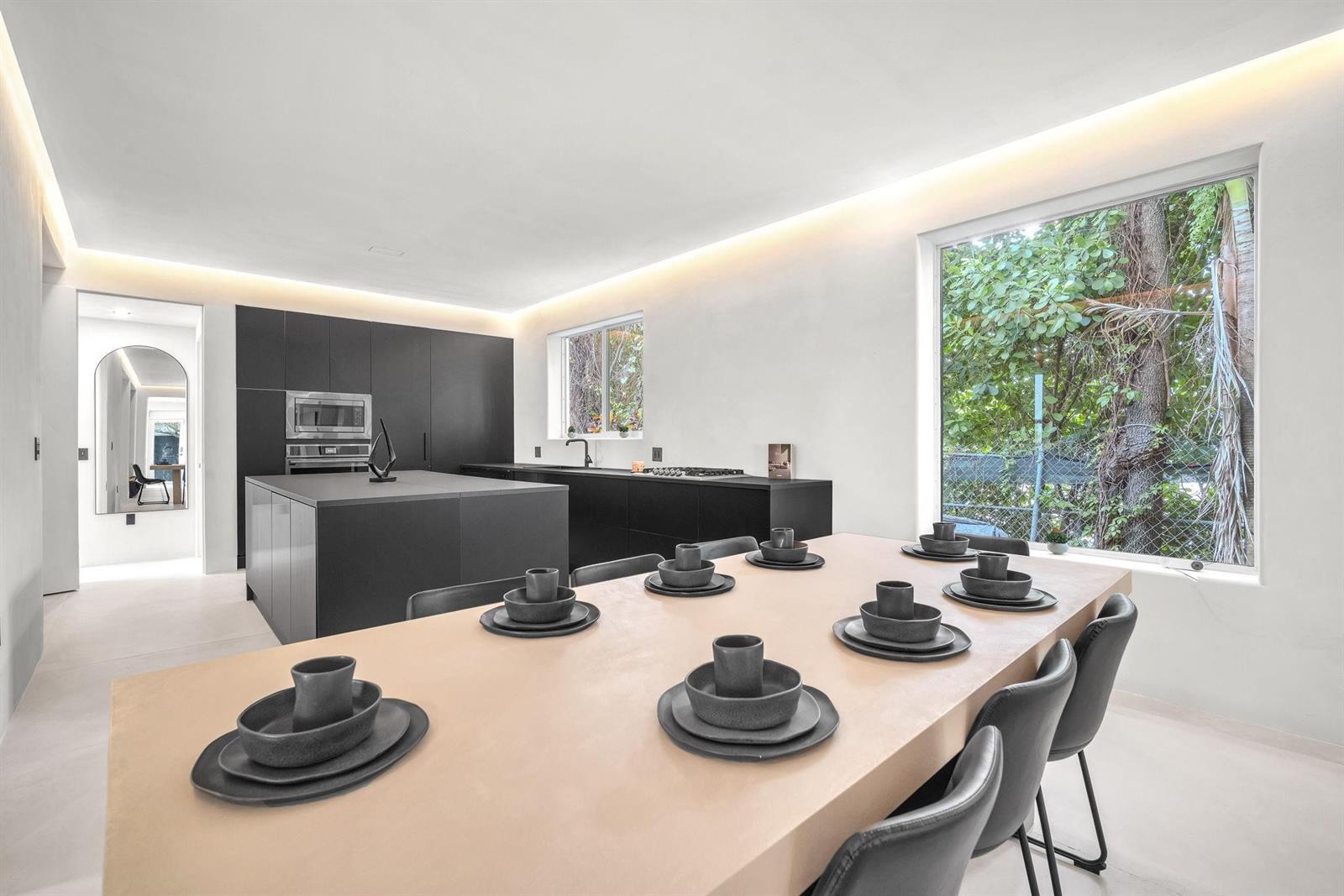 A modern kitchen and dining area features dark cabinetry, a light-colored table, and large windows — 120 NE 25th Street, Miami FL 33137, MIAMI, FL