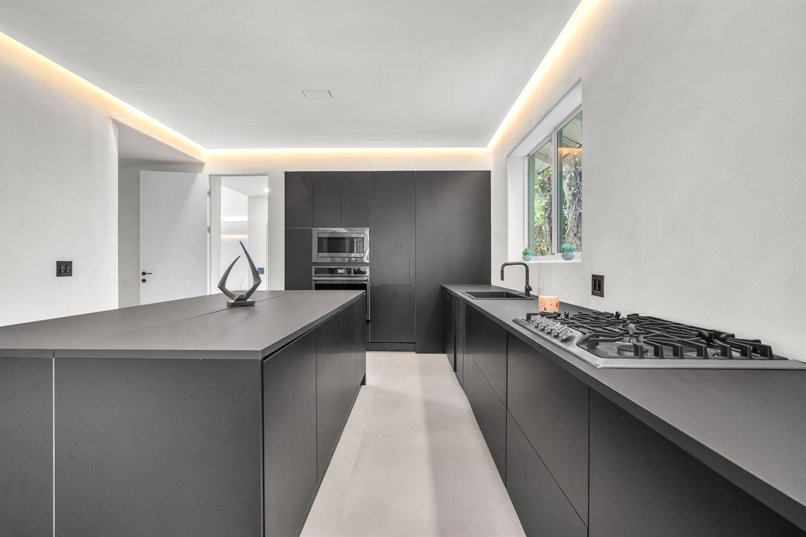 A modern kitchen features matte black cabinetry, a large island, and recessed cove lighting — 120 NE 25th Street, Miami FL 33137, MIAMI, FL