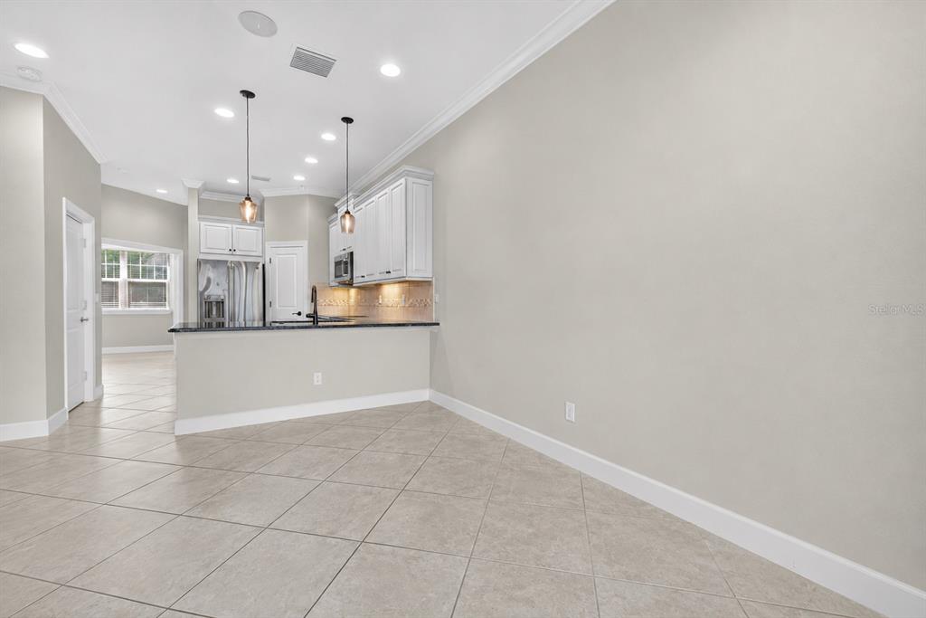 A kitchen with white cabinets, a granite island, and tile flooring opens to a dining area — 6080 MOORINGS DRIVE S, ST PETERSBURG, FL