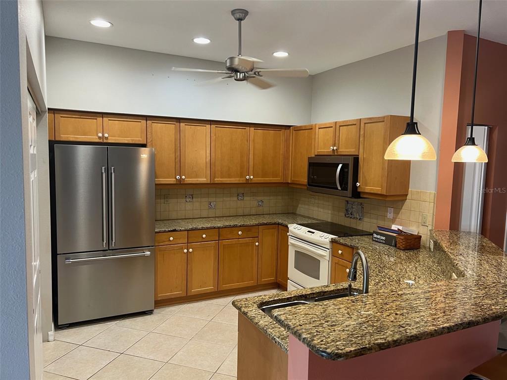 A kitchen features wood cabinets, granite countertops, stainless steel appliances, and a peninsula with sink — 6444 7TH AVENUE CIRCLE W UNIT 6444, BRADENTON, FL