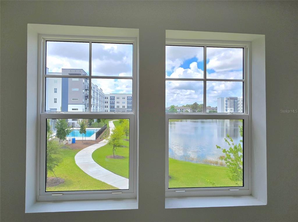 Two windows look out onto a grassy area, a swimming pool, and a pond — 5579 MILLENIA PARK BOULEVARD UNIT 211, ORLANDO, FL