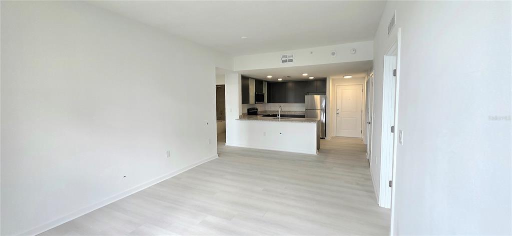 An open-concept living area features light wood-look flooring and a kitchen with dark cabinetry — 5579 MILLENIA PARK BOULEVARD UNIT 211, ORLANDO, FL