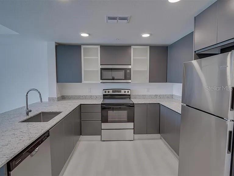 A modern kitchen features gray cabinets, stainless steel appliances, and speckled granite countertops — 5579 MILLENIA PARK BOULEVARD UNIT 211, ORLANDO, FL