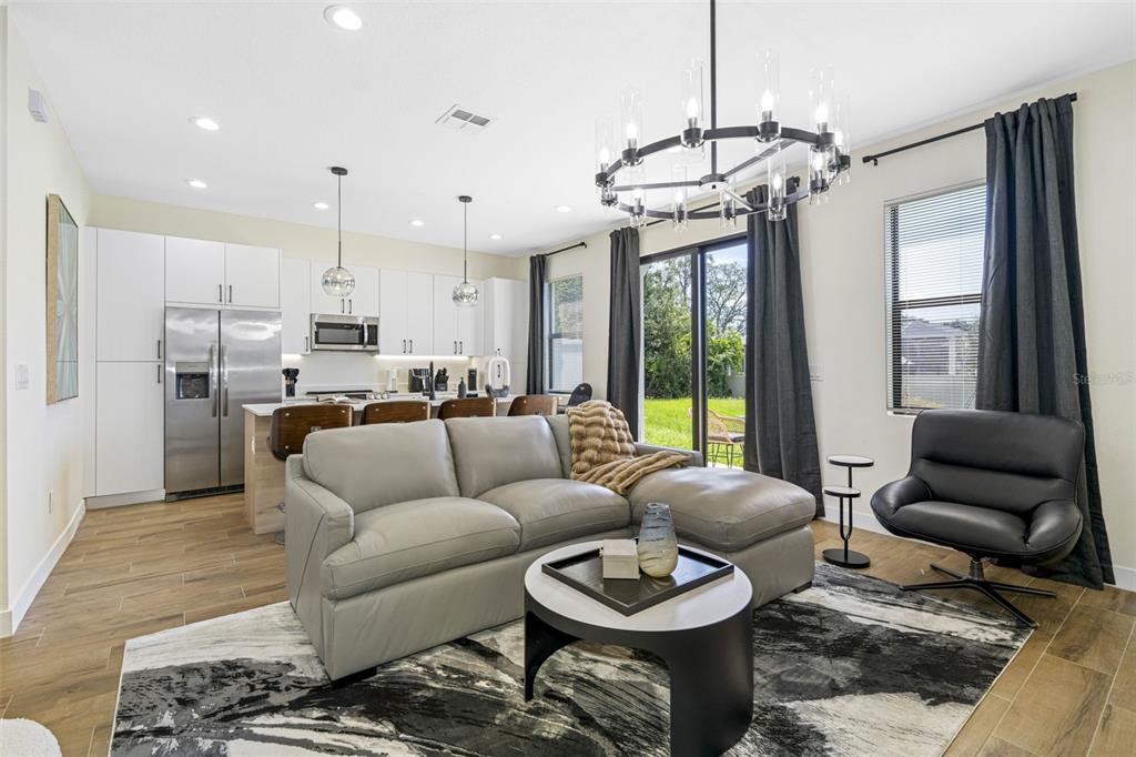 A modern open-concept living room and kitchen featuring a gray sectional, chandelier, and tile flooring — 4340 VILLA ALINA COURT, TAMPA, FL
