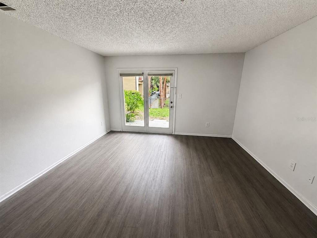 An empty room features light gray walls, dark wood-look flooring, and glass double doors — 249 AFTON SQUARE UNIT 107, ALTAMONTE SPRINGS, FL