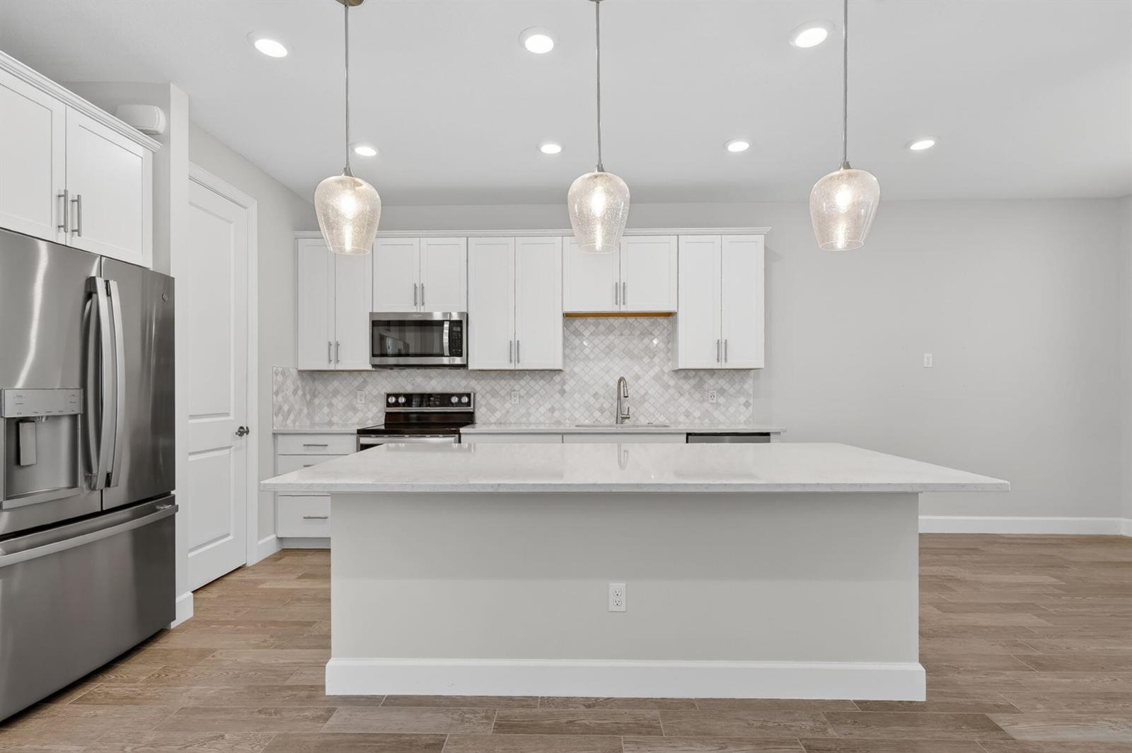 A modern kitchen features white cabinets, a large quartz island, stainless steel appliances, and pendants — 1887 SE Ocean Cove Way, Stuart FL 34996, STUART, FL