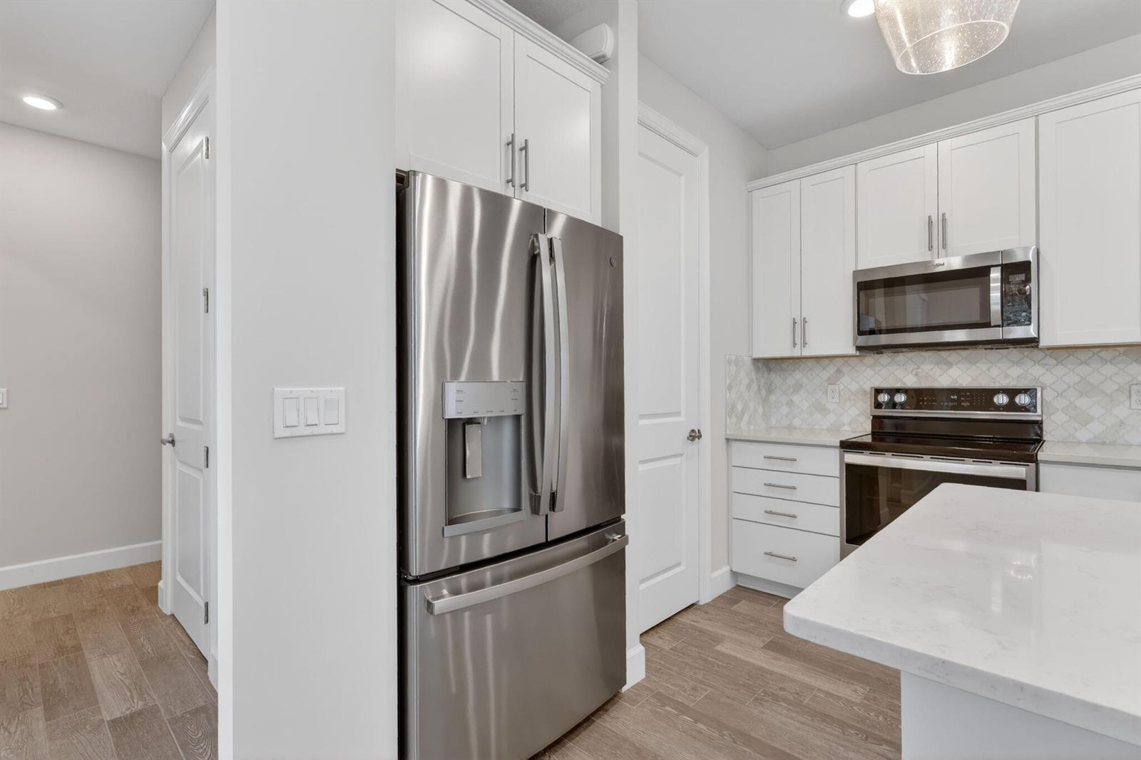 A modern kitchen features white cabinets, stainless steel appliances, and light wood-look flooring — 1887 SE Ocean Cove Way, Stuart FL 34996, STUART, FL