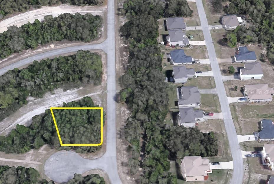 An aerial view shows a vacant, wooded lot outlined in yellow within a residential neighborhood — SARASOTA PLACE, POINCIANA, FL