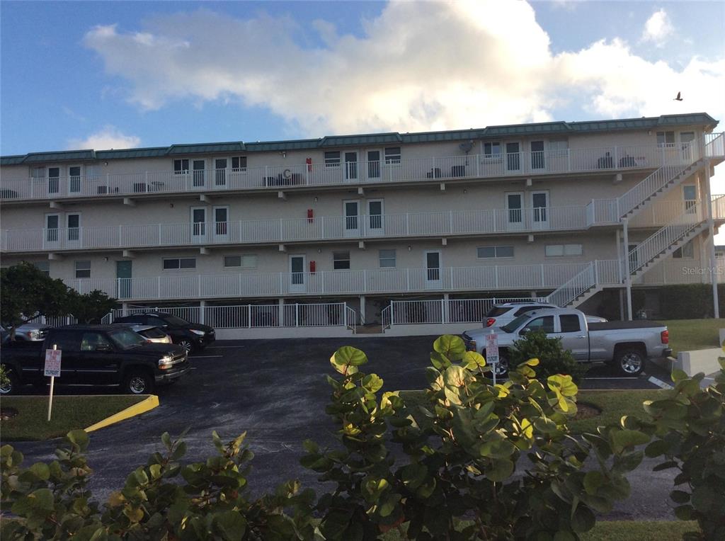 A three-story apartment building with exterior walkways and a parking lot in the foreground — 4849 SAXON DRIVE UNIT C102, NEW SMYRNA BEACH, FL