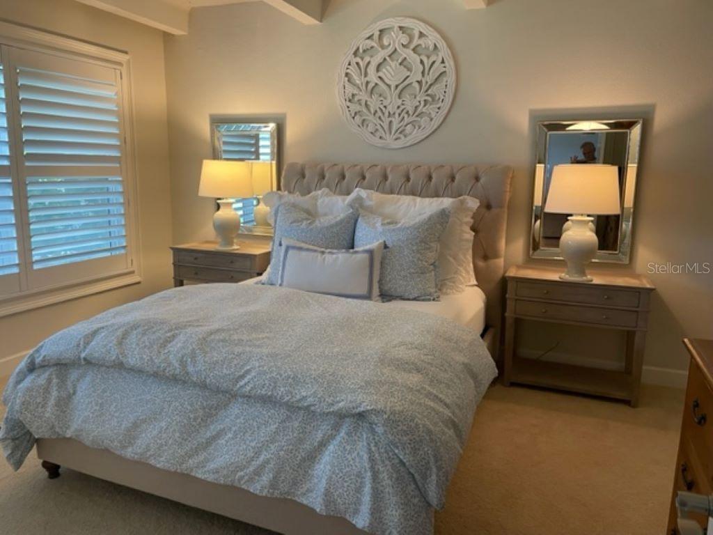 A bedroom features a tufted headboard, two nightstands with lamps, and a circular wall decoration — 4849 SAXON DRIVE UNIT C102, NEW SMYRNA BEACH, FL
