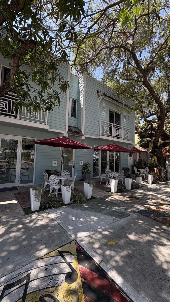A light blue two-story building features outdoor patio seating with red umbrellas and white furniture — 3872 Grand Ave # A, Miami FL 33133, MIAMI, FL