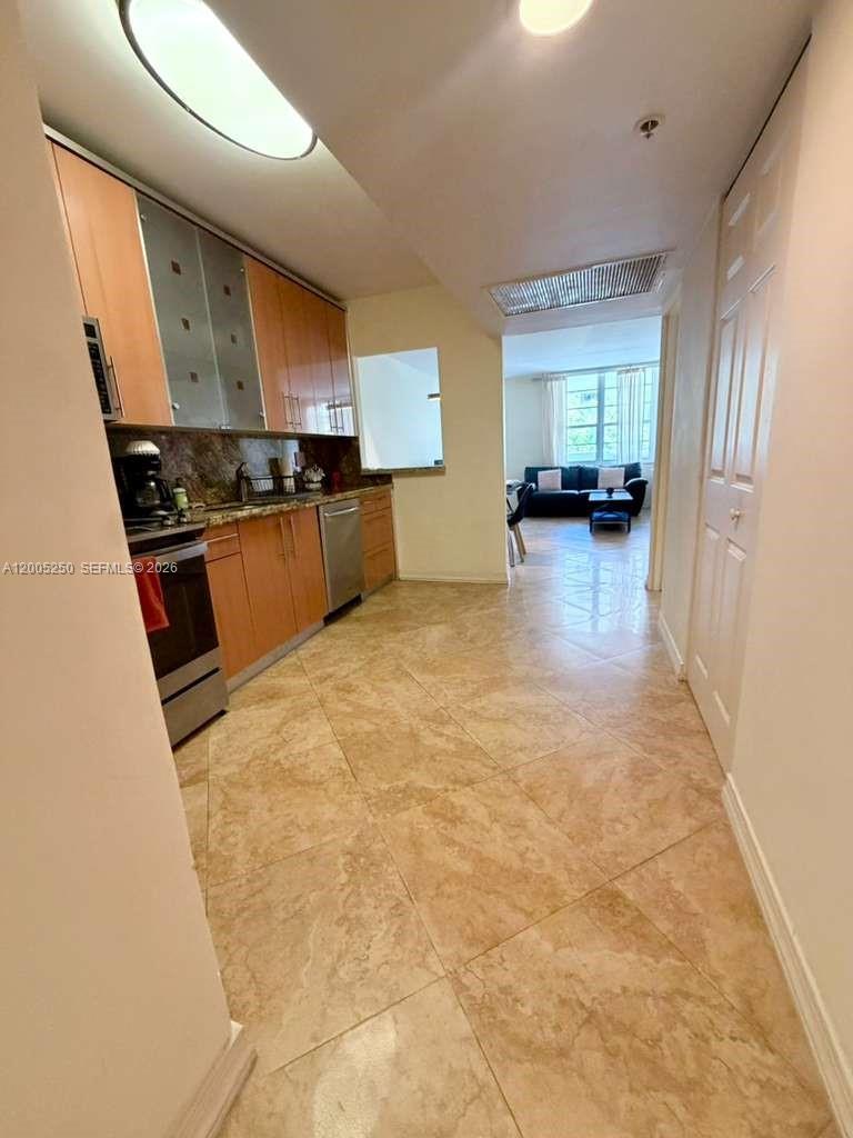 A galley kitchen with wood cabinets and tile flooring leads into a living area — 100 Lincoln Rd # 534, Miami Beach FL 33139, MIAMI BEACH, FL