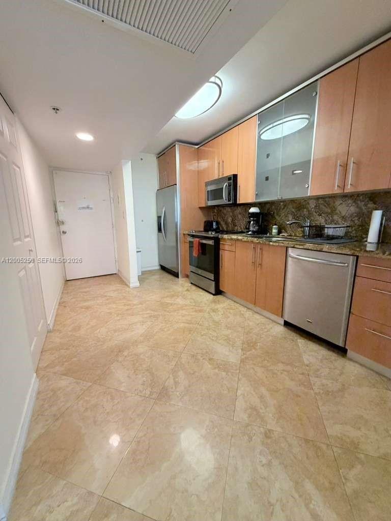 A kitchen features light wood cabinets, stainless steel appliances, and beige tile flooring — 100 Lincoln Rd # 534, Miami Beach FL 33139, MIAMI BEACH, FL