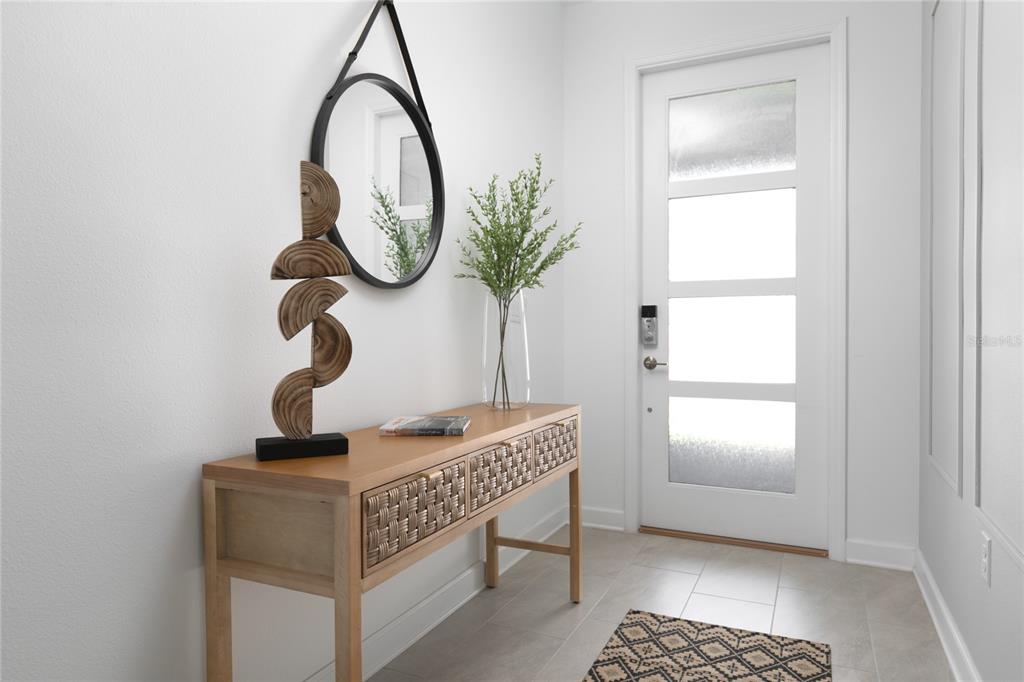 A bright entryway features a wooden console table, a round mirror, and a modern front door — 4290 PARAGRAPH DR, KISSIMMEE, FL