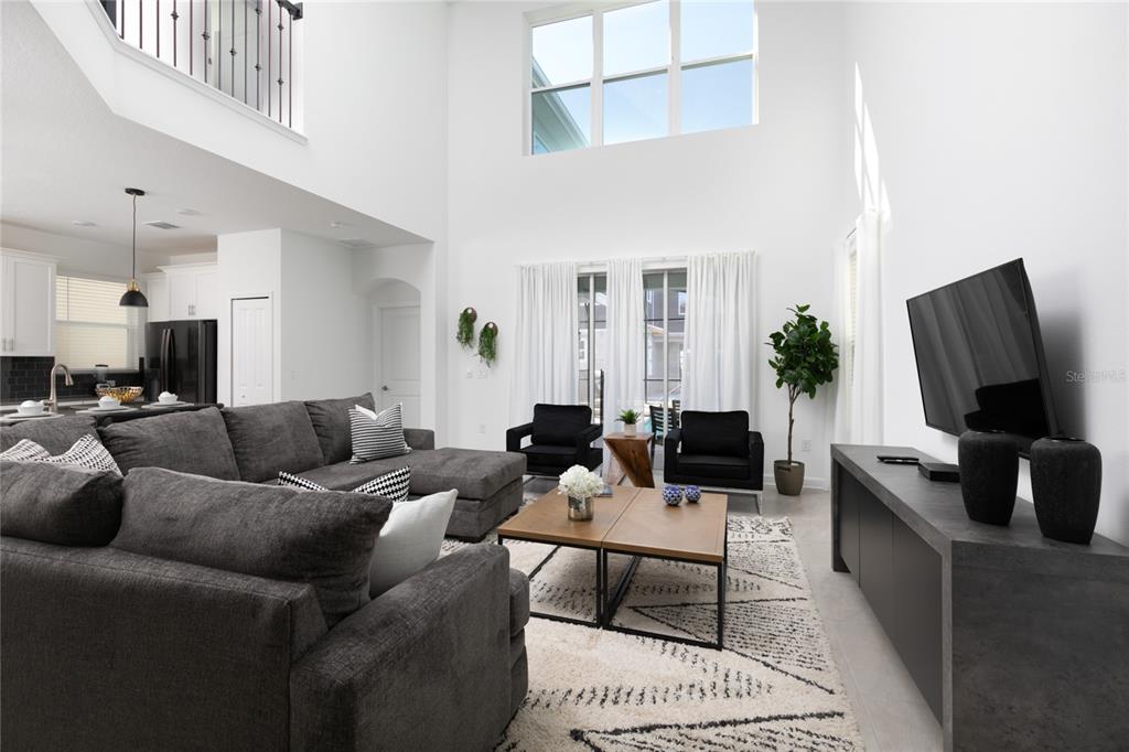 A high-ceilinged living room features a gray sectional sofa, two black armchairs, and a television — 4290 PARAGRAPH DR, KISSIMMEE, FL