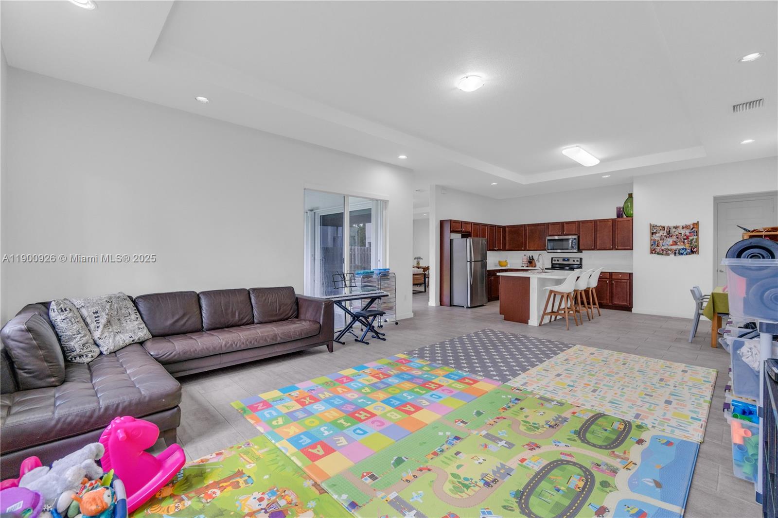 This open-concept living area features a brown leather sectional, play mats, and a kitchen — 15288 SW 176th Ter, Miami FL 33187, MIAMI, FL
