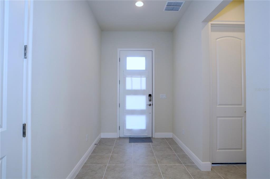 An entryway features light-colored walls, tiled flooring, a white front door, and a closed door — 5174 BUTTONSAGE DRIVE, ST CLOUD, FL
