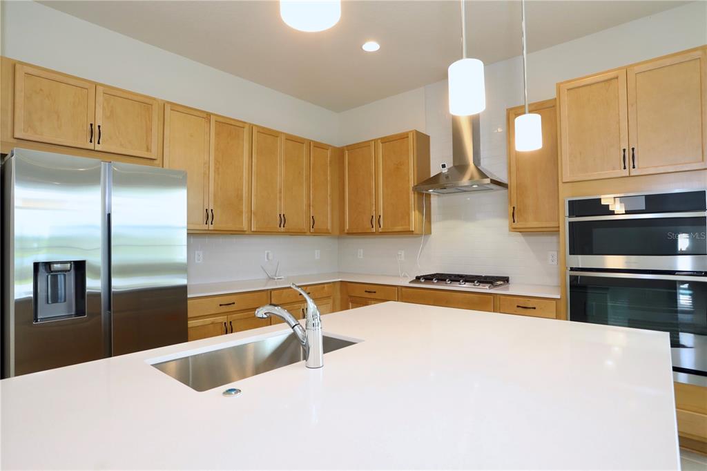 A modern kitchen features light wood cabinets, a white quartz island, and stainless steel appliances — 5174 BUTTONSAGE DRIVE, ST CLOUD, FL