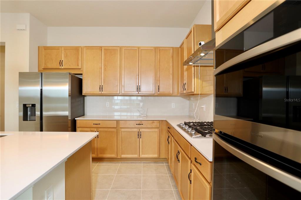 A kitchen features light wood cabinets, stainless steel appliances, white countertops, and tile flooring — 5174 BUTTONSAGE DRIVE, ST CLOUD, FL