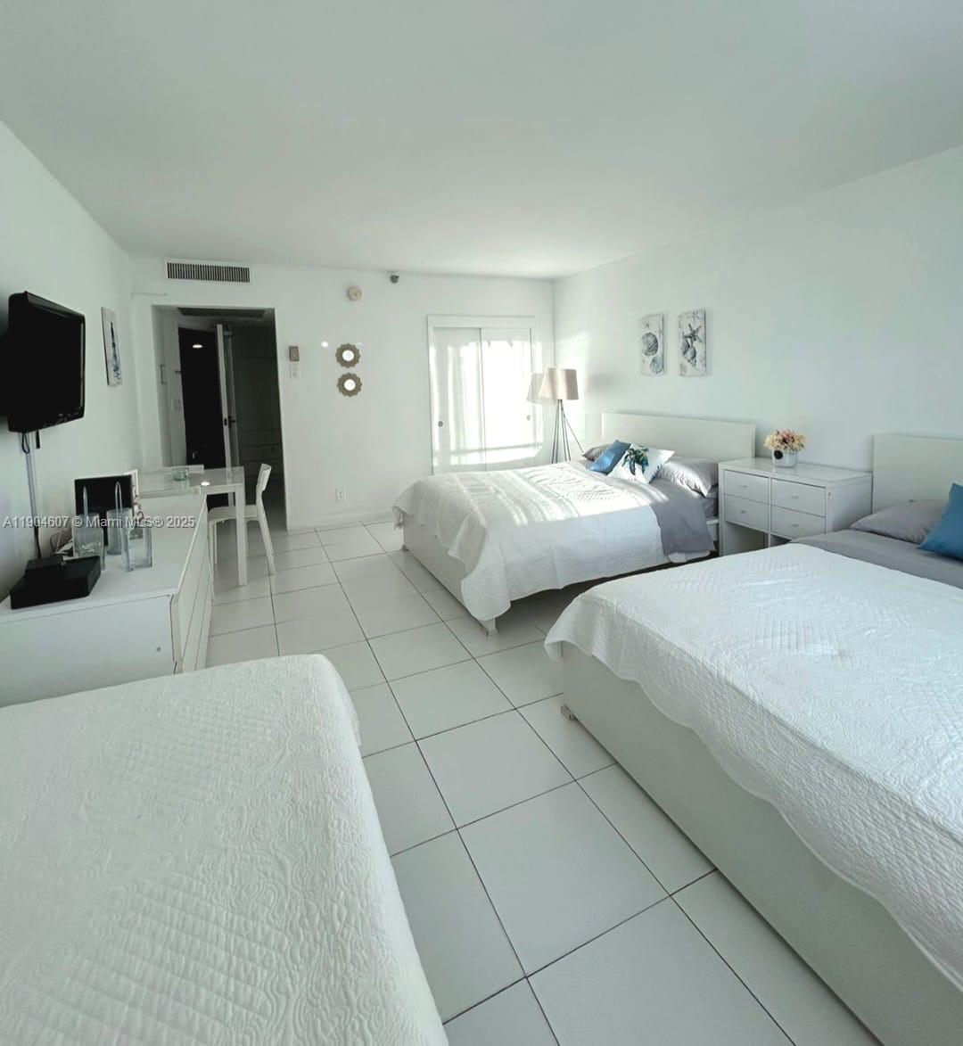 A bedroom with white tile floors, two beds, a dresser, and a small dining area — 5445 Collins Ave # 617, Miami Beach FL 33140, MIAMI BEACH, FL