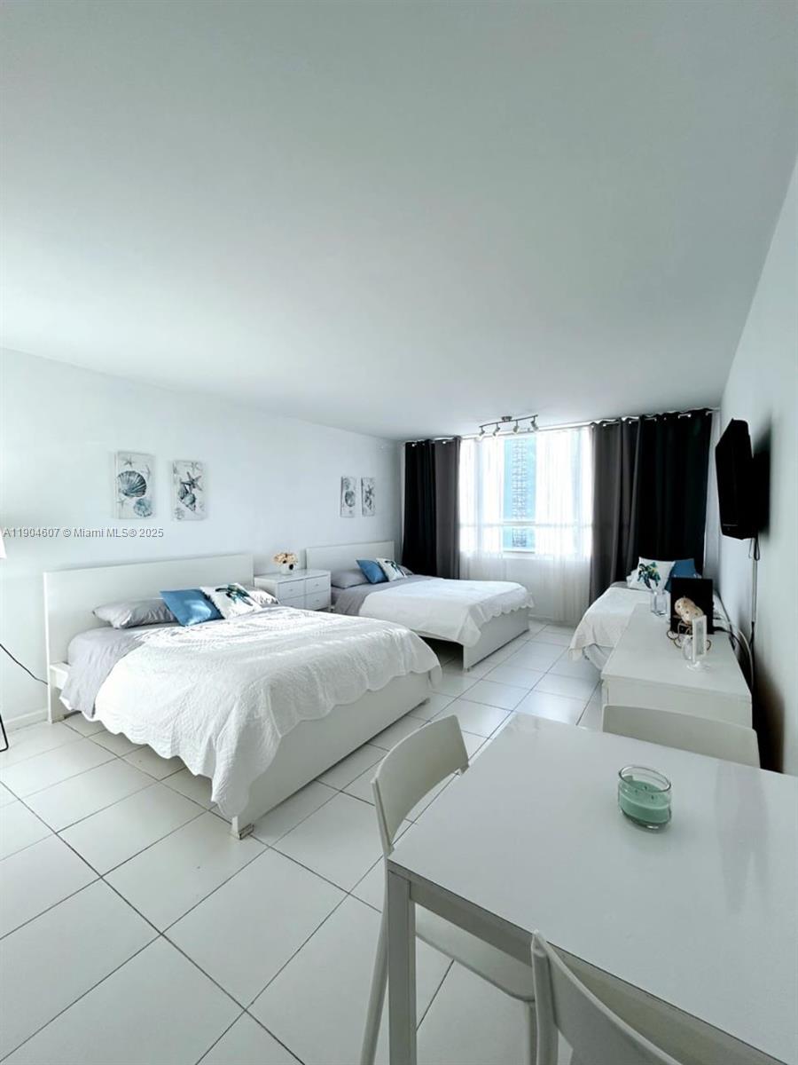 A bedroom features two white beds, a small dining table, and large window curtains — 5445 Collins Ave # 617, Miami Beach FL 33140, MIAMI BEACH, FL