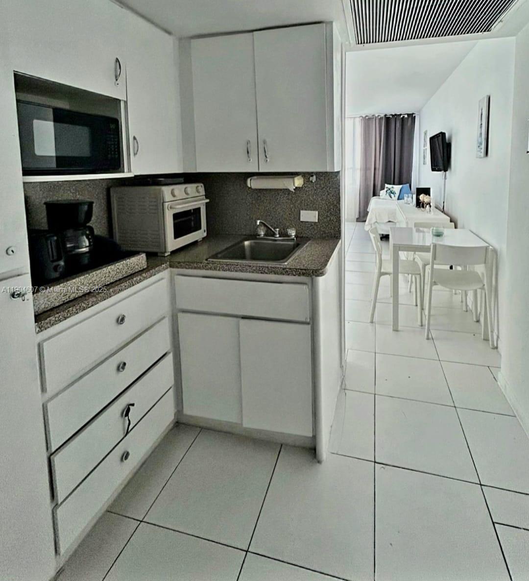 A small kitchen with white cabinets and a speckled countertop leads into a dining area — 5445 Collins Ave # 617, Miami Beach FL 33140, MIAMI BEACH, FL