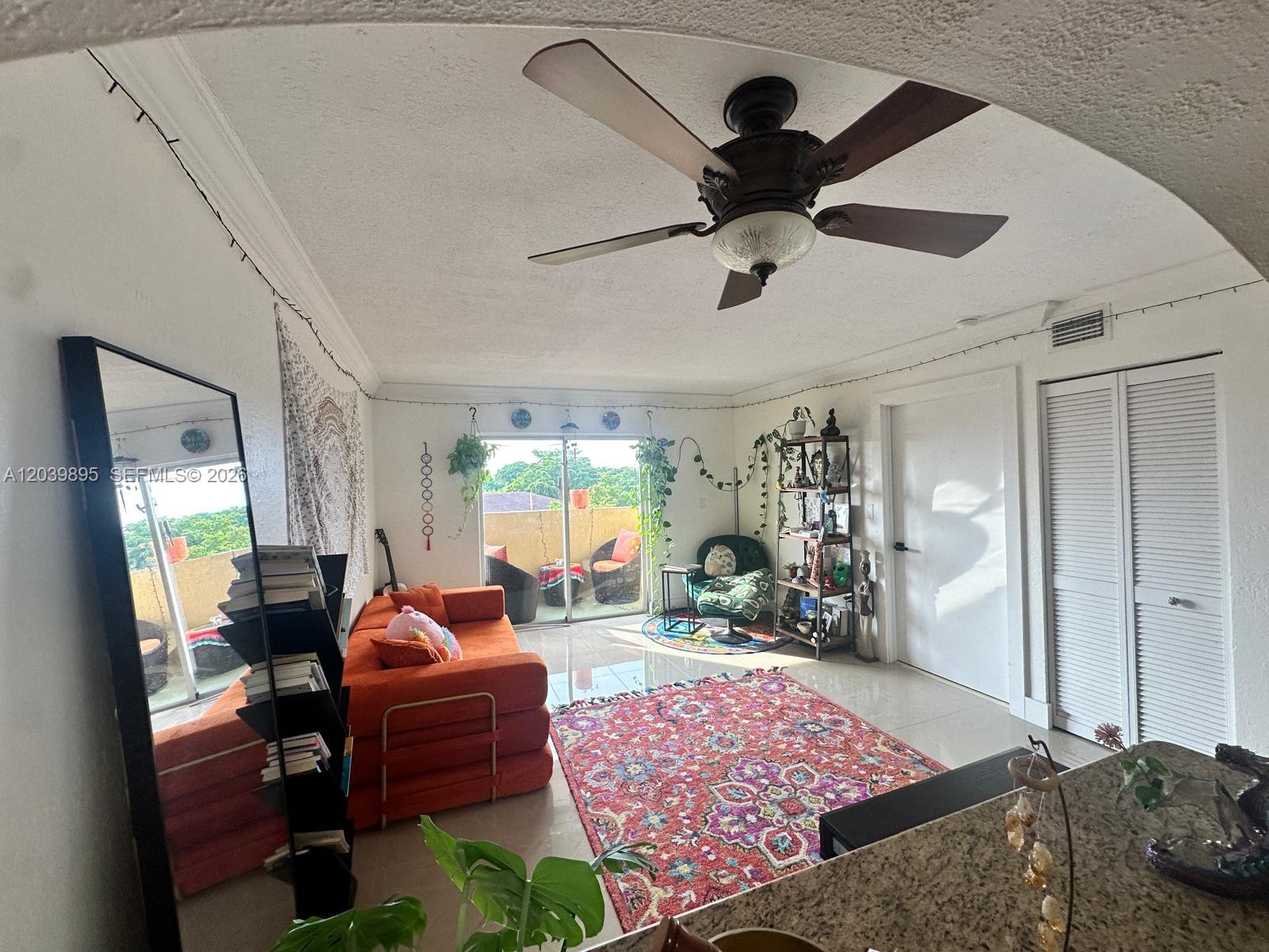 A living room features an orange sofa, a patterned rug, and a balcony with greenery — MIAMI, FL