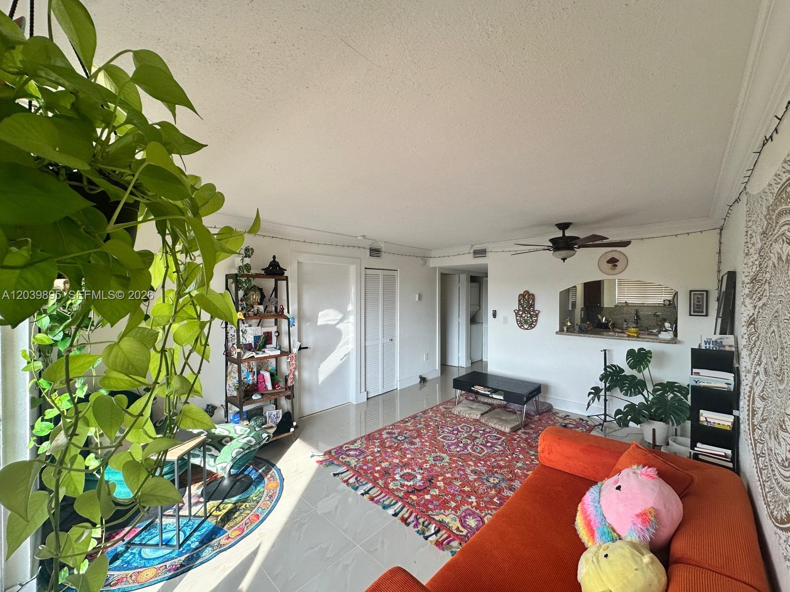 A living room features a large orange sofa, a patterned area rug, and a hanging plant — MIAMI, FL