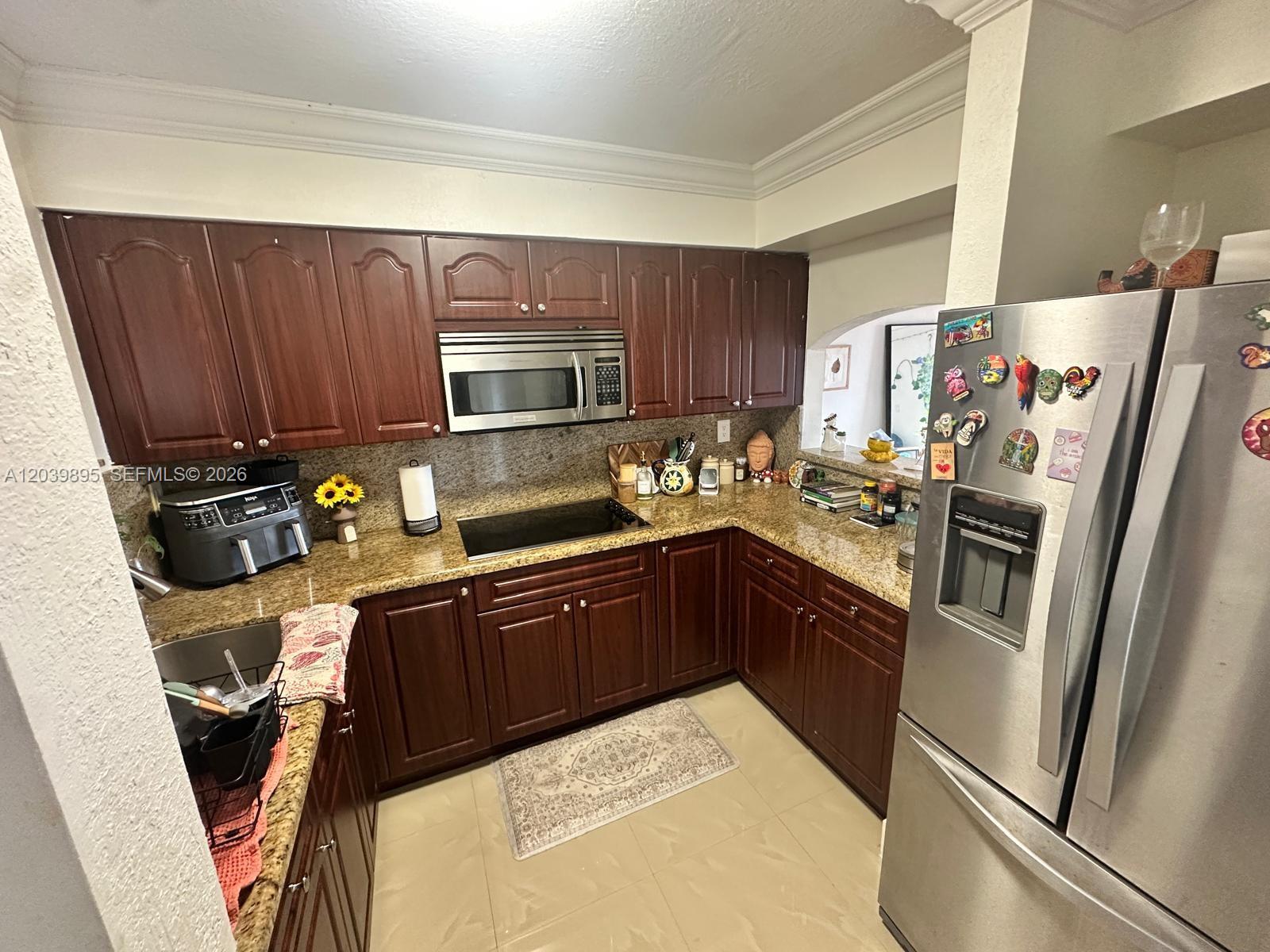 A kitchen features dark wood cabinets, granite countertops, stainless steel appliances, and tile flooring — MIAMI, FL