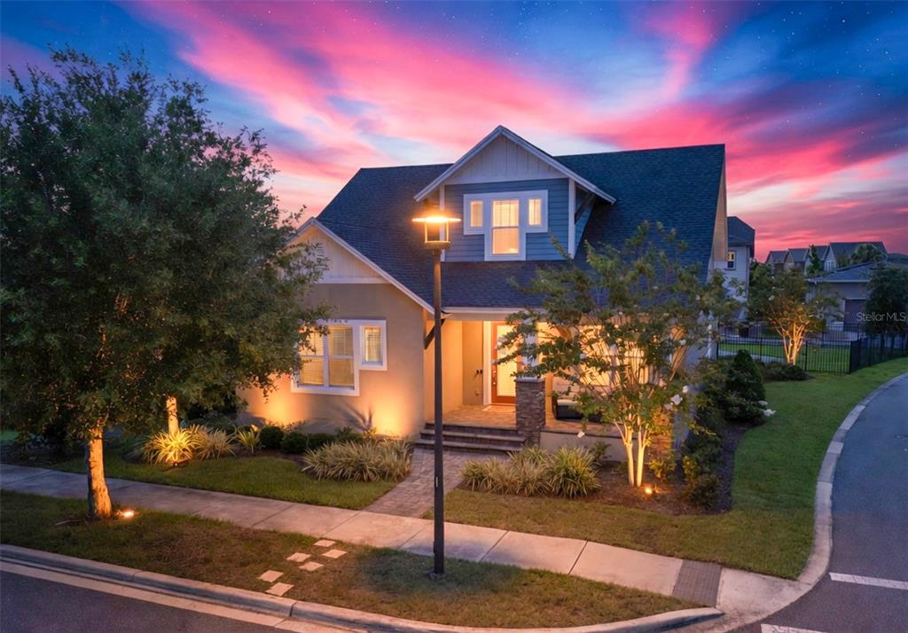 A two-story house with a blue-trimmed gable, front porch, and illuminated landscaping at sunset — 13347 GABOR AVENUE, ORLANDO, FL
