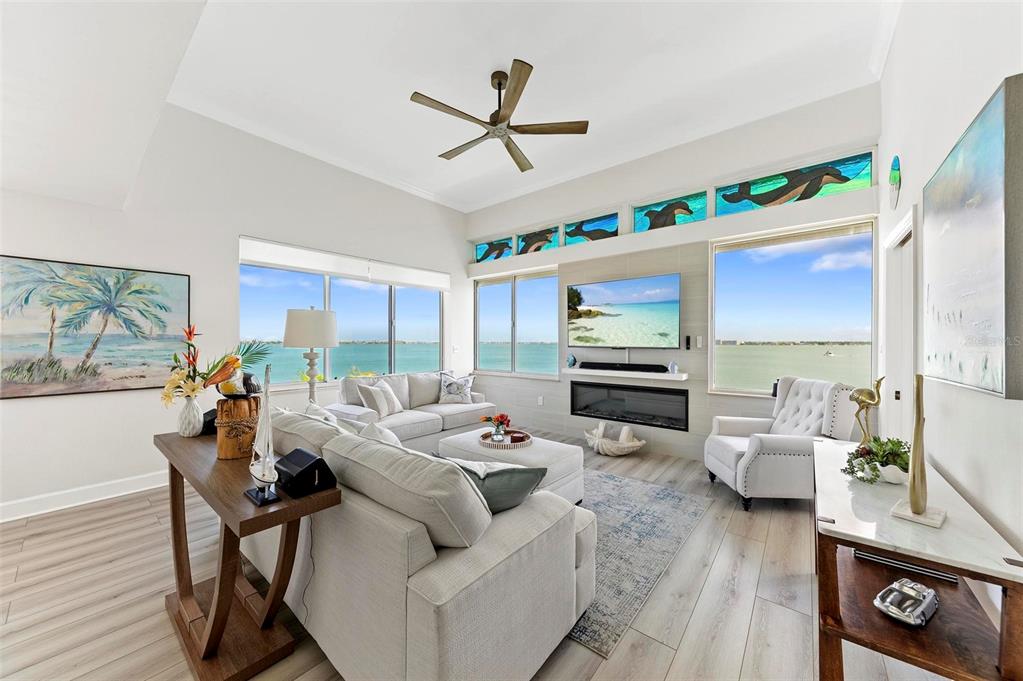 A bright living room features a fireplace, wall-mounted television, and expansive water views — 5153 ISLA KEY BOULEVARD S UNIT 408, ST PETERSBURG, FL