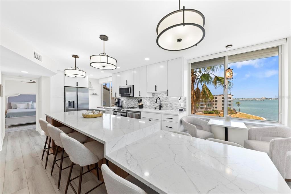 A modern kitchen features white cabinetry, marble-topped counters, and a large window overlooking the water — 5153 ISLA KEY BOULEVARD S UNIT 408, ST PETERSBURG, FL