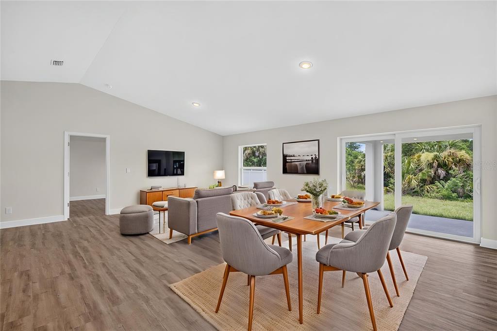 An open-concept living and dining area features light wood flooring, vaulted ceilings, and sliding doors — 147 FLANDERS STREET, PORT CHARLOTTE, FL