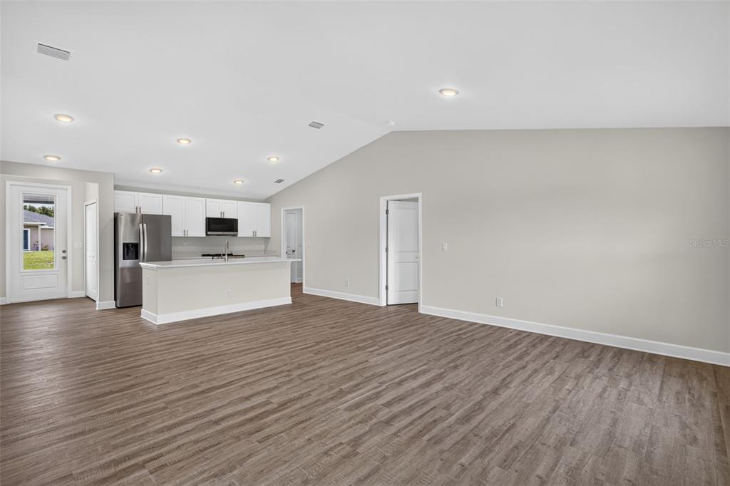 An open-concept living area features wood-look flooring, a vaulted ceiling, and a kitchen with white cabinets — 147 FLANDERS STREET, PORT CHARLOTTE, FL
