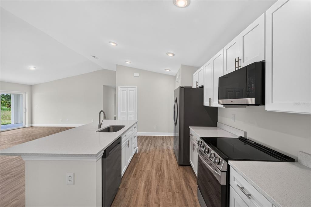 A modern kitchen features white cabinets, stainless steel appliances, and a quartz-topped island — 147 FLANDERS STREET, PORT CHARLOTTE, FL