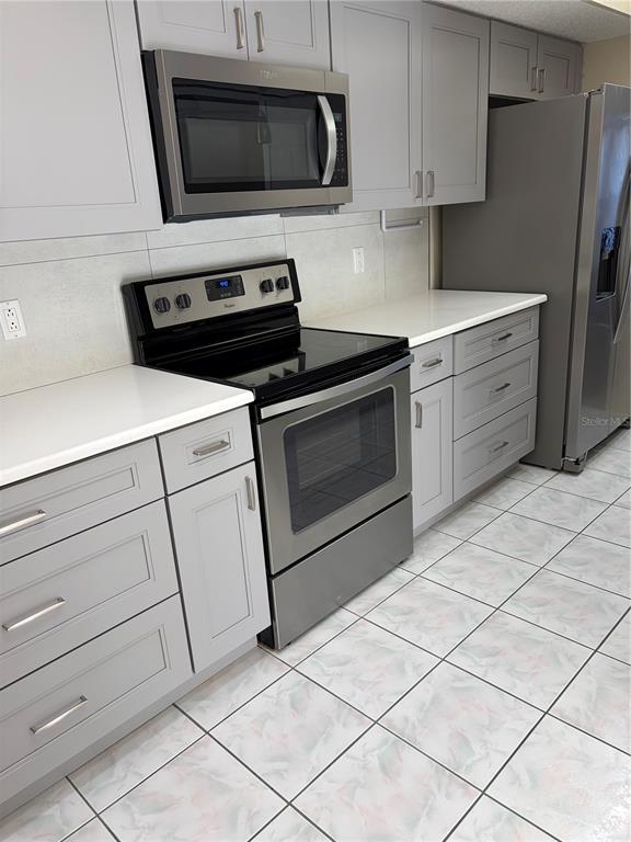 A kitchen features gray cabinets, stainless steel appliances, white countertops, and light-colored tiled flooring — 3807 STAYSAIL LANE UNIT 3807, HOLIDAY, FL