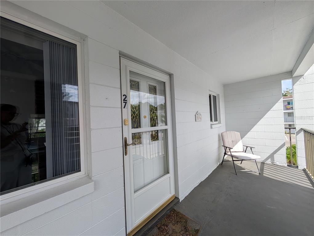 A white exterior wall features a front door numbered 27, a window, and a patio chair — 5896 GARDEN LANE UNIT A27, BRADENTON, FL