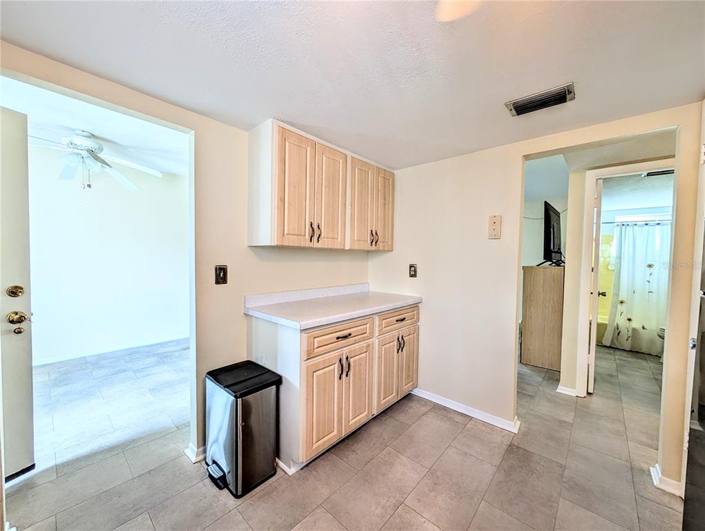 A kitchen area features light wood cabinets, a white countertop, and gray tile flooring — 5896 GARDEN LANE UNIT A27, BRADENTON, FL