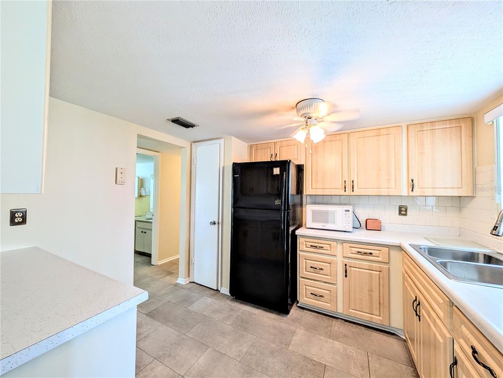 A kitchen features light wood cabinets, a black refrigerator, and gray tile flooring — 5896 GARDEN LANE UNIT A27, BRADENTON, FL