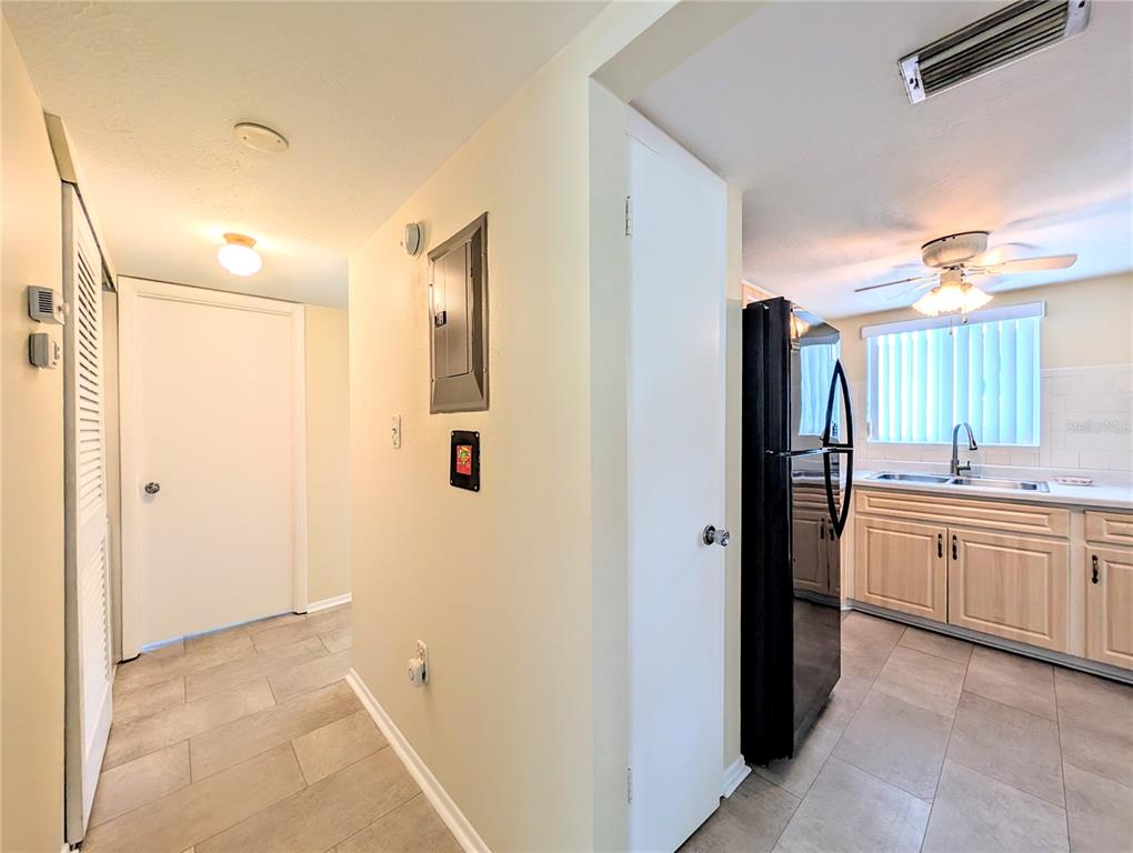 A hallway with tile flooring leads to a kitchen featuring light wood cabinets and appliances — 5896 GARDEN LANE UNIT A27, BRADENTON, FL