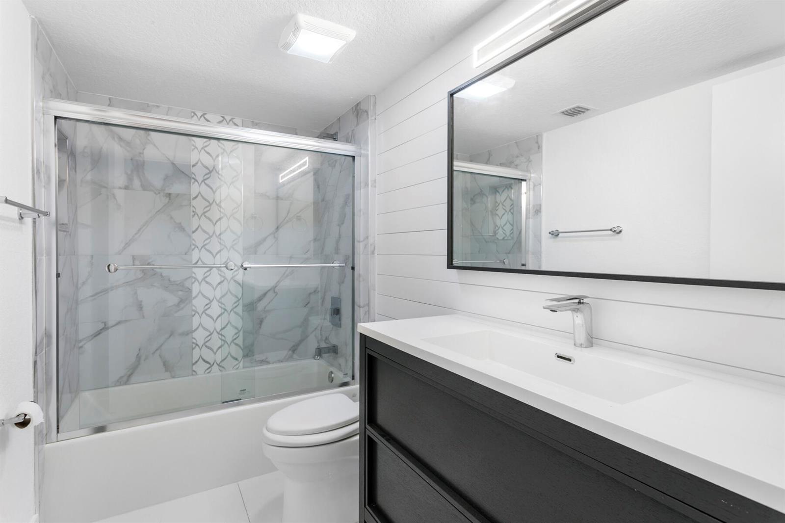 A modern bathroom features a dark vanity, white shiplap walls, and a glass-enclosed tub shower — 601 Seafarer Circle # 101, Jupiter FL 33477, JUPITER, FL