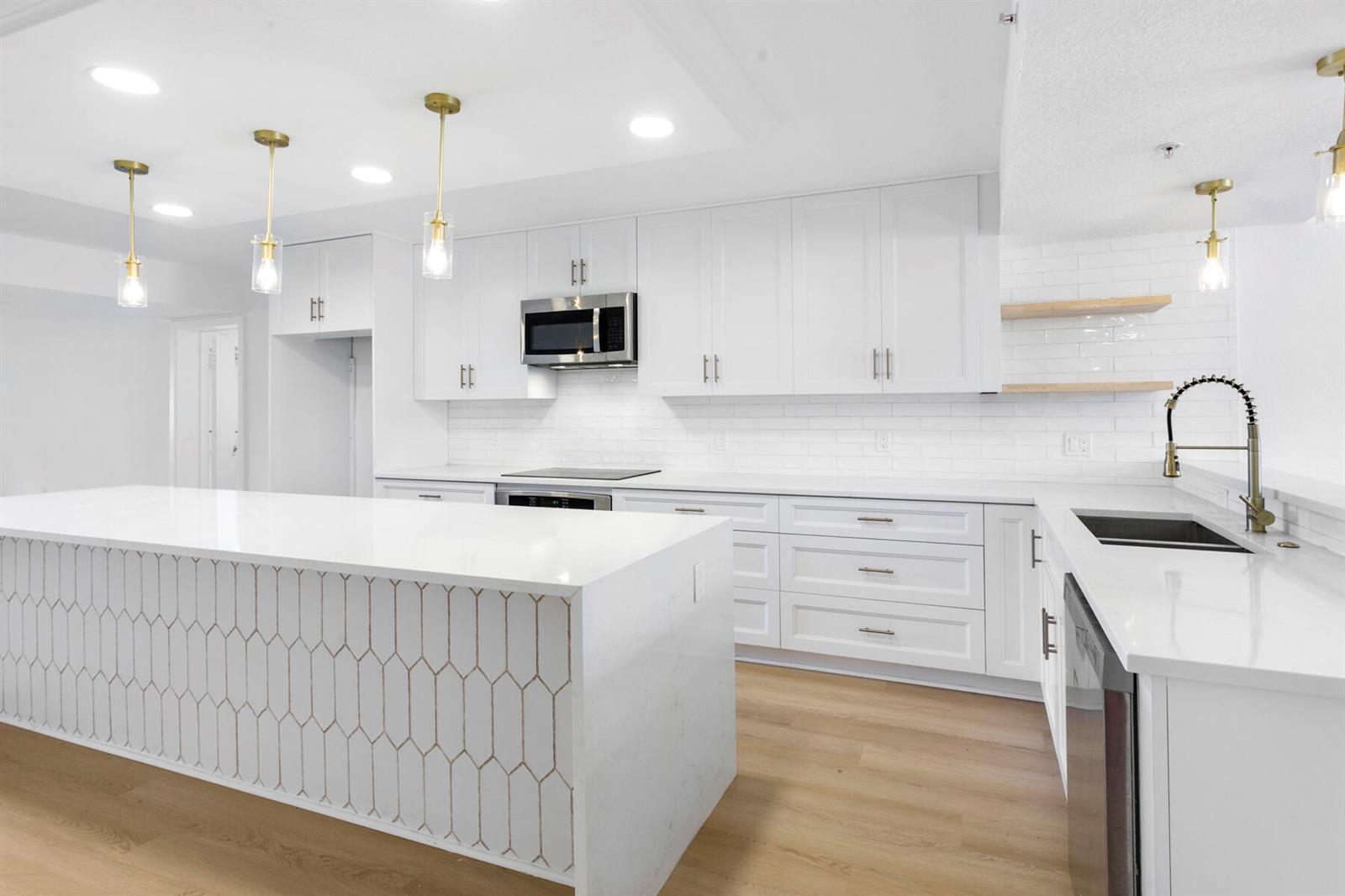 A modern white kitchen features a large island with geometric tile, quartz countertops, and gold fixtures — 601 Seafarer Circle # 101, Jupiter FL 33477, JUPITER, FL