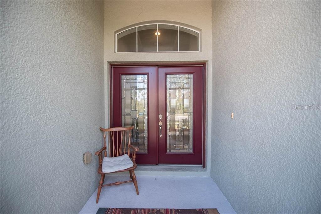 A wooden chair sits on a concrete porch in front of double red entry doors — 1742 MIRA LAGO CIRCLE, RUSKIN, FL